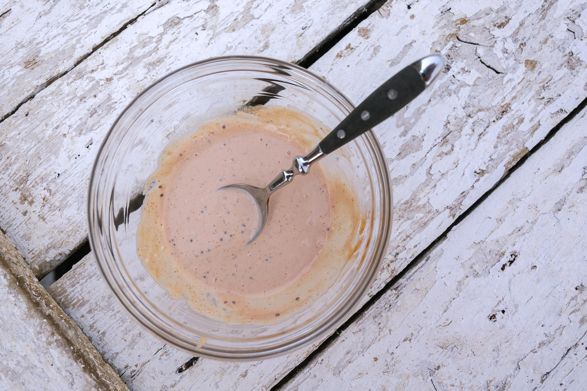 Die Mayonnaise mit dem Ketchup, Senf und Schmand verrühren. Mit Salz, Pfeffer und 1 EL Gurkenwasser aus dem Glas abschmecken. (Quelle: Dorn/DJV)