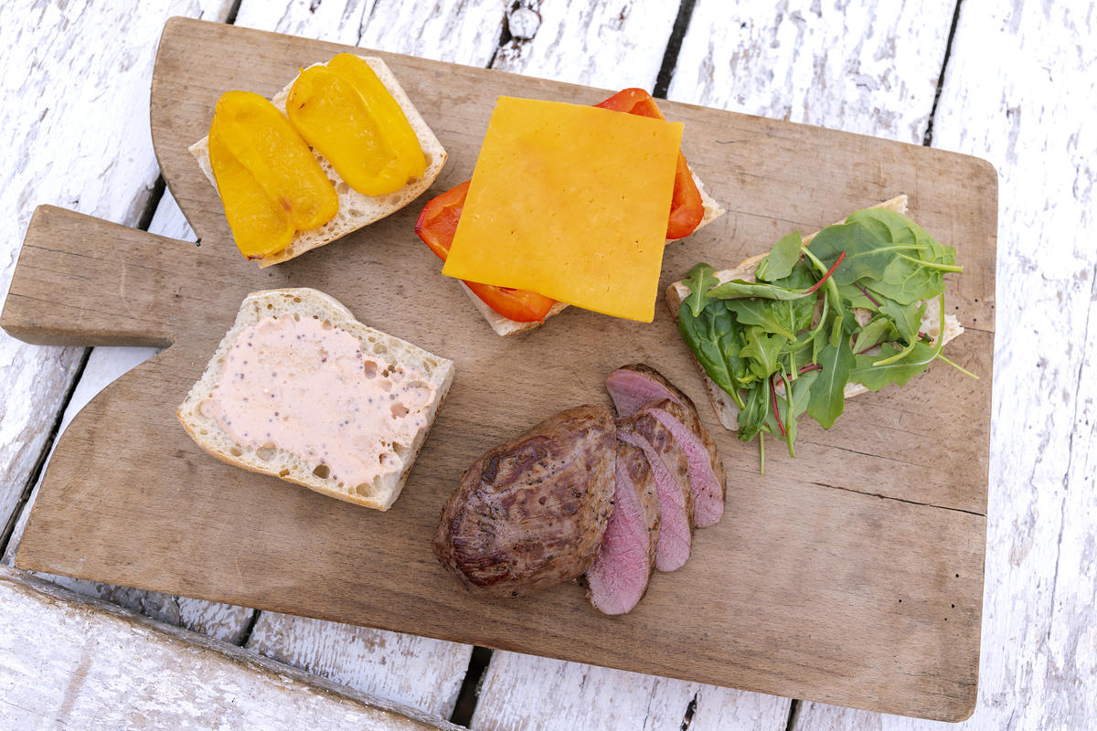 Fleisch in dünne Scheiben schneiden. Die unteren Baguettescheiben mit dem Dressing bestreichen. Darauf den Salat und das Fleisch verteilen. Mit Parmesanhobeln garnieren. (Quelle: Dorn/DJV)