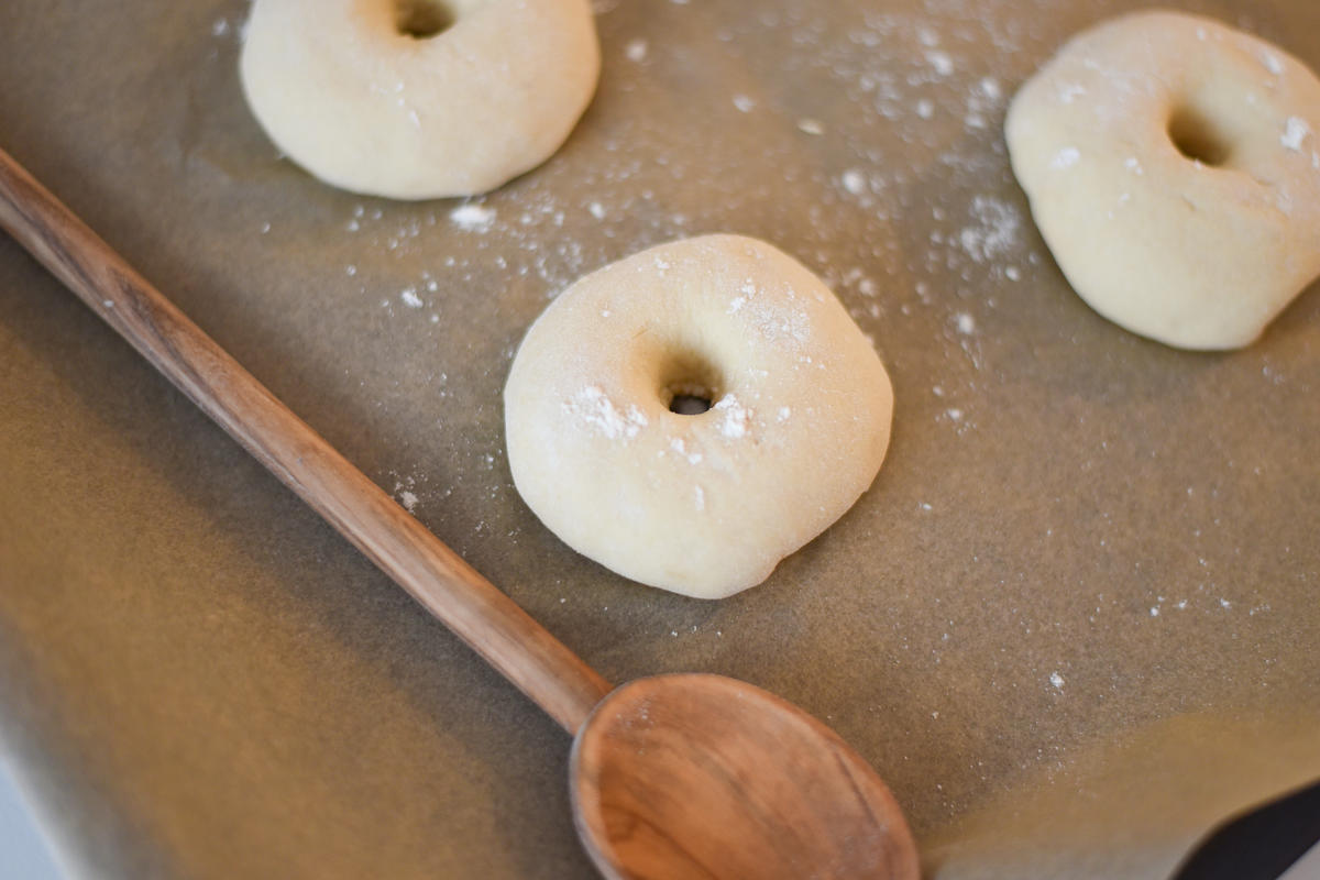 In die Mitte des Teigs ein fingerbreites Loch stechen, zum Beispiel mit dem Stiel eines Kochlöffels. Die Bagel nun erneut abgedeckt auf ein mit Backpapier ausgelegtes Backblech geben und für eine halbe Stunde ruhen lassen. (Quelle: Kapuhs/DJV )