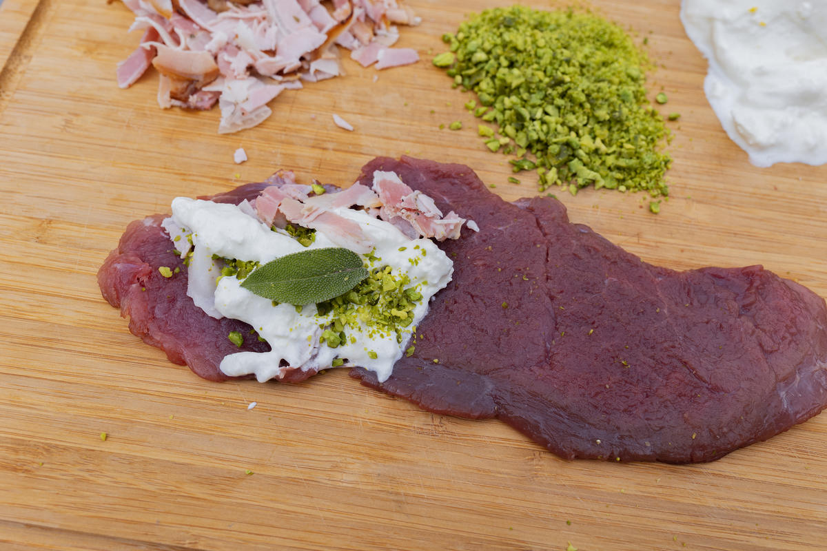 Schnitzel auf der einen Seite mit ein paar Schinken- und Mozzarellawürfeln belegen. Pistazienkerne drüberstreuen. Schnitzel zuklappen und mit Holzspießchen fixieren. (Quelle: Dorn/DJV)