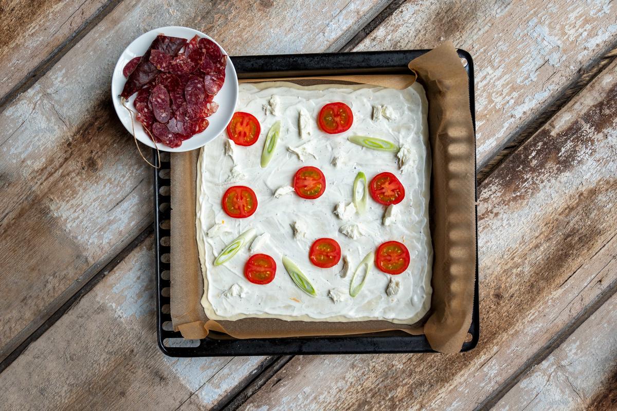 Mit Tomatenscheiben, Frühlingszwiebeln und etwas klein gezupftem Mozzarella belegen. Flammkuchen in den Ofen schieben. Nach ein paar Minuten herausnehmen mit der Wildschweinsalami belegen.  (Quelle: Dorn/DJV)