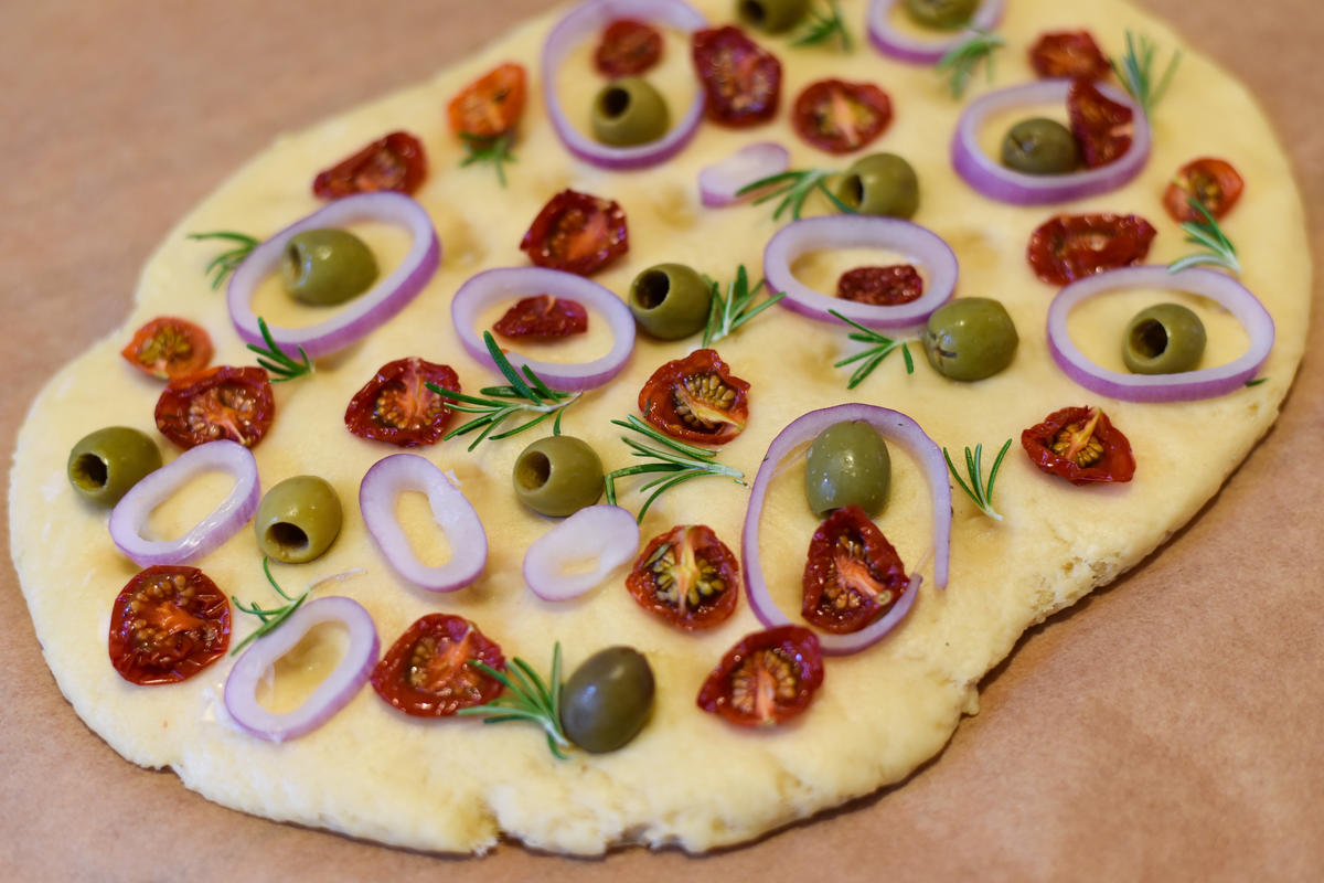 Für das Focaccia Mehl, Salz, Butter, Milch und Hefe mischen. Ruhen lassen und mit Tomaten, Oliven, Zwiebeln und Rosmarin belegen. Im Backofen für 25 bis 30 Minuten backen.  (Quelle: Kapuhs/DJV )