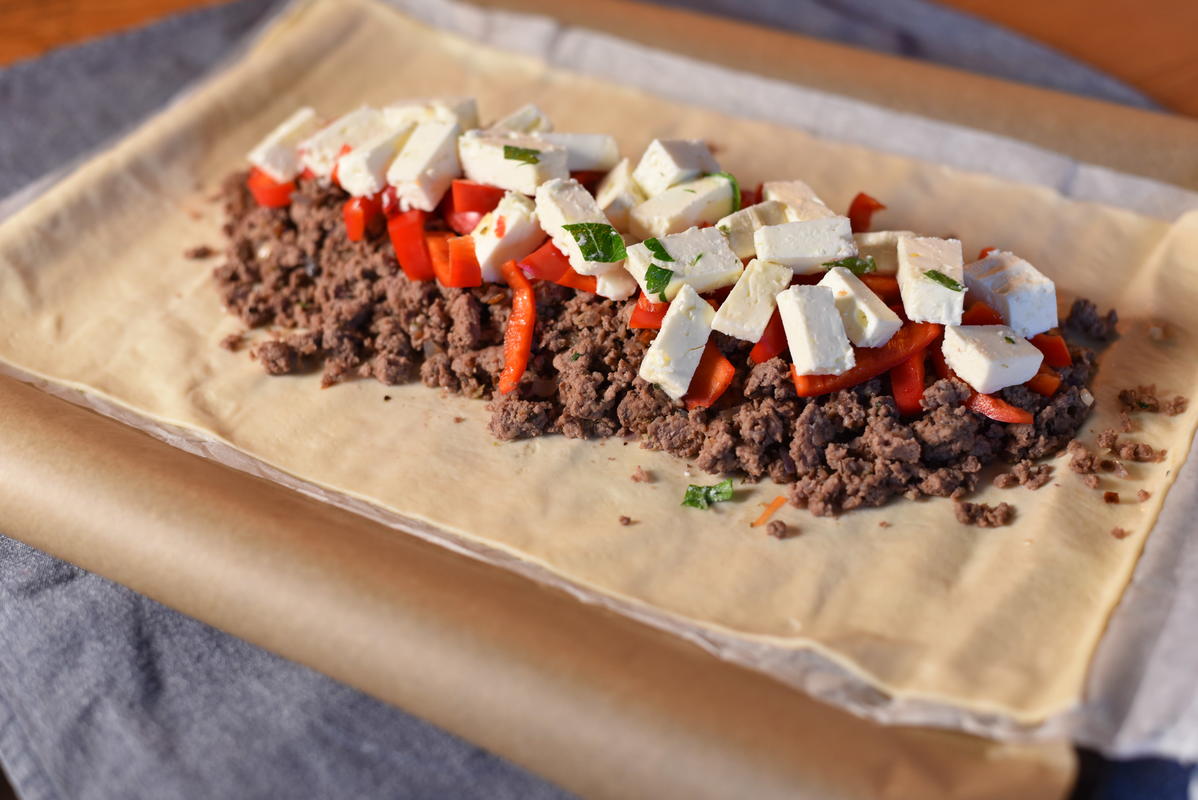 Hackfleisch, gewürfelte Paprika und Schafskäse auf den ausgerollten Blätterteig geben. (Quelle: Kapuhs/DJV)