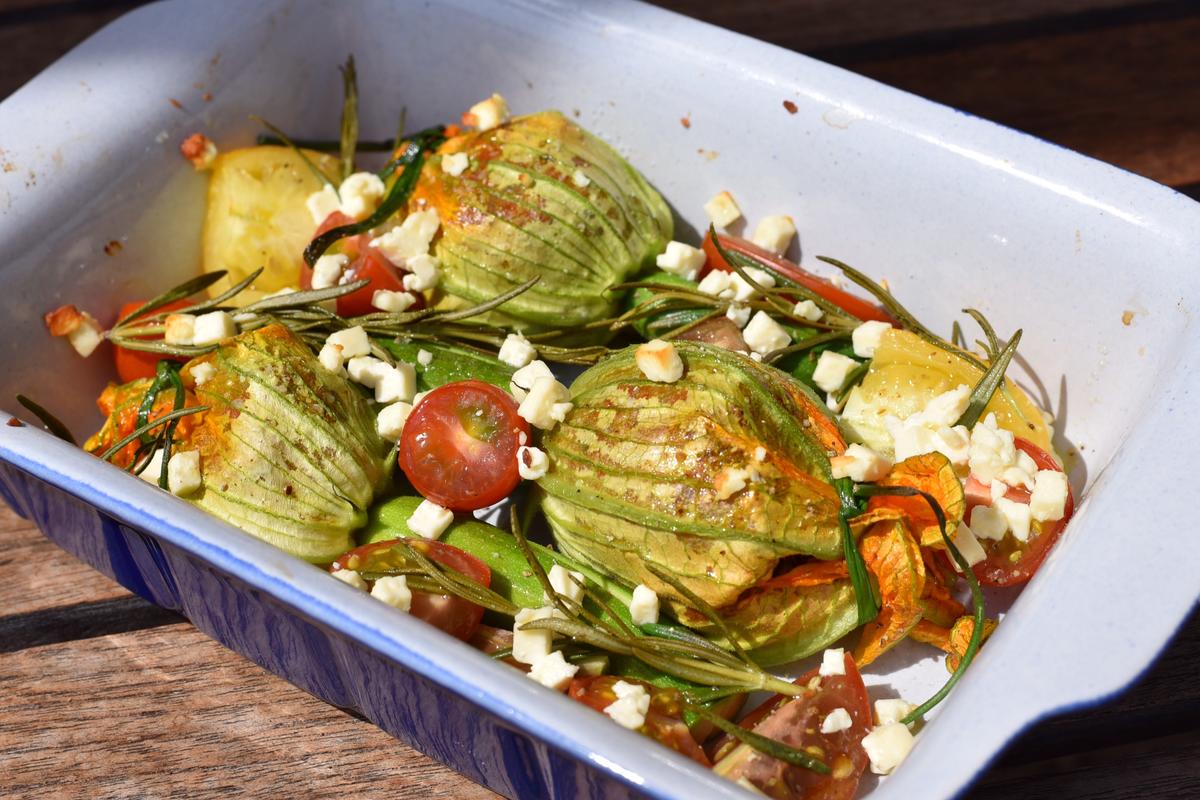 Zucchiniblüten, Tomaten und Rosmarin in Auflaufform geben. Mit Öl beträufeln, salzen, pfeffern und mit Fetakäse bestreuen. Für zirka 15 Minuten backen. (Quelle: Kapuhs/DJV)